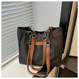 Detail of minimalist black tote bag with brown leather straps and silver metal chain