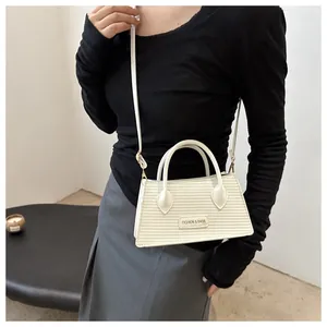 Detail of cream woven textured handbag featuring golden metal brand plaque and round handle