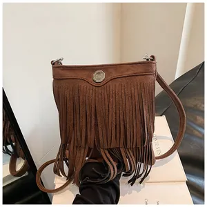 Detail of dark brown suede crossbody bag featuring long fringes and a round metal buckle