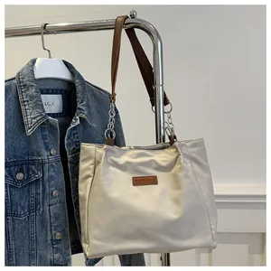 Detail of cream tote bag featuring brown leather handles and decorative metal chain