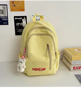 Detail of yellow school backpack with HOKEAM embroidery and plush bear pendant