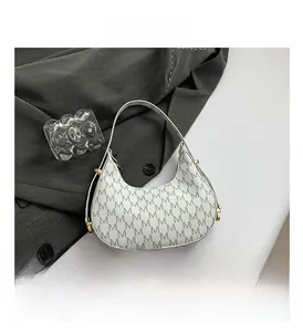 Close-up of white crescent bag with M monogram pattern and gold metal hardware