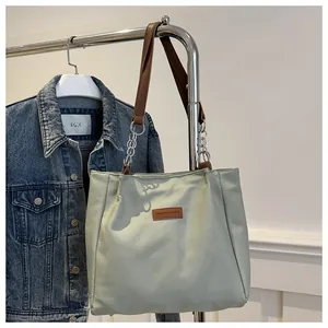 Detail of light green tote bag with brown leather straps and silver metal chain links