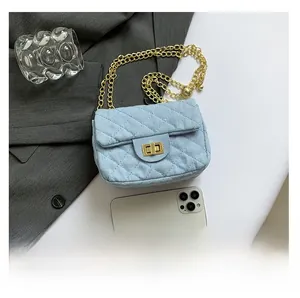 Detail of light blue quilted denim crossbody bag with gold chain strap and turn-lock