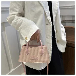 Close-up of light pink woven mini handbag featuring leather handles and brand patch