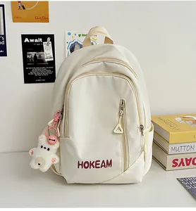 Detail of cream backpack with HOKEAM logo, side pocket, and cute plush bear charm