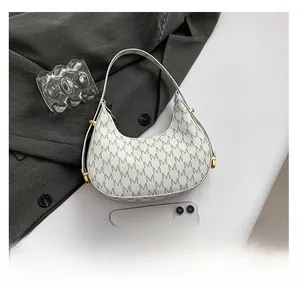 Close-up of white hobo bag with M-pattern print and gold hardware next to a smartphone
