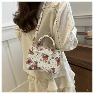 Detail of white butterfly print crossbody bag shown worn by a model in elegant setting