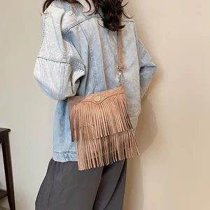 Brown fringe crossbody bag with suede texture and metal buckle on a bohemian style model