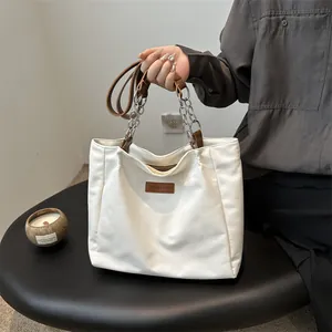 Minimalist white tote bag with metal chain strap and leather trim on a black table