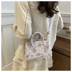 Detail of a white crossbody bag with pink butterfly patterns shown on a female model