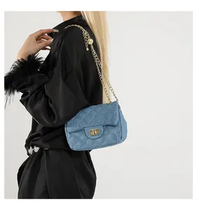 Detail of blue quilted denim crossbody bag with gold chain strap and turn-lock closure