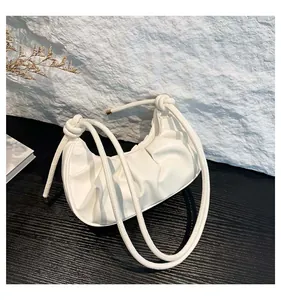 Detailed view of white pleated crescent bag with knotted rope shoulder strap detail