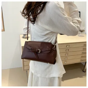 Detail van donkerbruine leren crossbodytas met gouden gesp en riem op het model