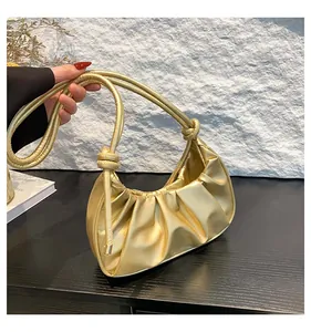 Close-up of golden pleated cloud bag with knotted cord handle against a stone wall