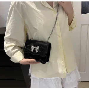 Detail of black bow chain bag with pleated texture shown on a female model