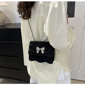 Detail of black velvet crossbody bag with silver bow buckle and wavy edge on chain strap