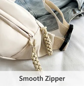 Detail shot of the smooth double zippers with woven pulls and plastic buckle on cream crossbody bag