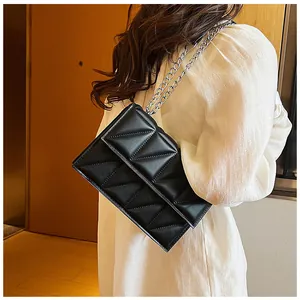 Détail du sac à bandoulière matelassé noir avec chaîne argentée sur robe blanche