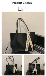 Detail view of large black tote bag with decorative silk scarf beside a laptop