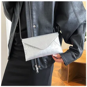 Detail of silver envelope bag featuring skull embossing and black metal chain strap
