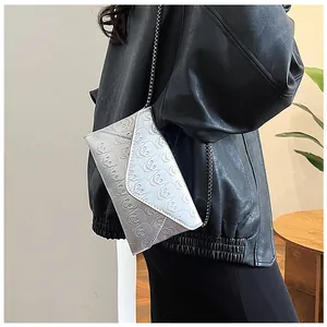 Detail of silver skull-embossed envelope bag with a sleek metal chain on model