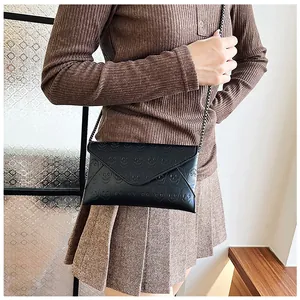 Close-up of black envelope crossbody bag with skull embossing and metal chain strap