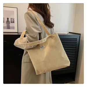 Detailed texture of beige corduroy tote bag with woven label and wide shoulder straps