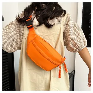 Detail of bright orange crossbody bag with woven zipper pull and adjustable buckle strap