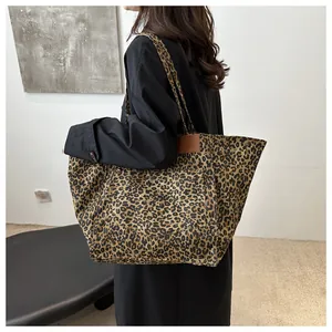 Leopard print canvas tote bag with brown leather handles shown on a model's shoulder