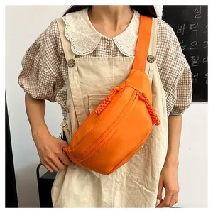 Detail of bright orange nylon waist bag featuring woven rope zipper pulls on crossbody strap