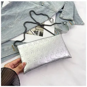Close-up of silver skull embossed pattern and metallic chain on an envelope clutch bag