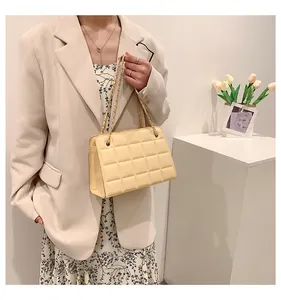 Dettaglio borsa trapuntata crema con catena dorata abbinata a un completo beige