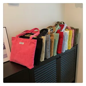 Multiple colors of corduroy tote bags with fashion labels on black storage shelves