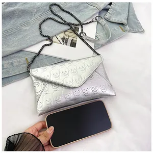Silver skull-embossed envelope bag next to a smartphone for size comparison