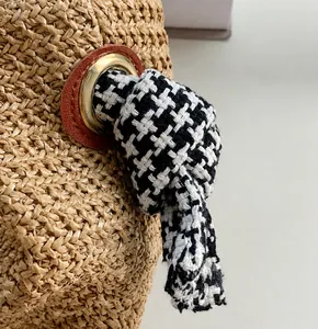 Detail of straw woven bag with golden eyelets and houndstooth fabric strap
