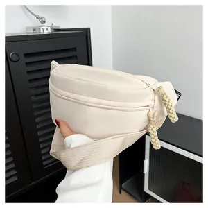 Close-up of minimalist cream crossbody bag showing woven rope zipper pulls and texture