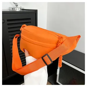 Close-up of bright orange nylon crossbody waist bag with woven zipper pull detail