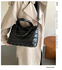 Detail of black quilted puffer tote bag with shoulder strap worn by a model in a trench coat