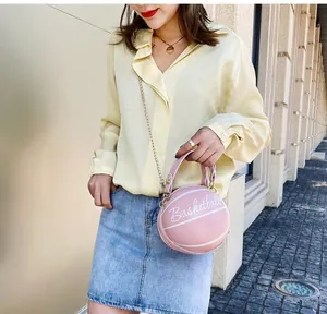 Photo de rue d'un sac chaîne rose en forme de basket tenu par un mannequin en chemise jaune