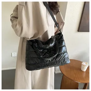 Detailed view of a black glossy quilted puffer bag with a wide adjustable nylon strap
