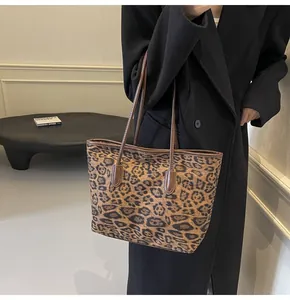 Detailed view of leopard print tote bag with brown leather handles worn with a black coat