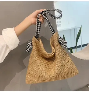 Detail of the woven straw handbag featuring stylish black and white houndstooth bow straps