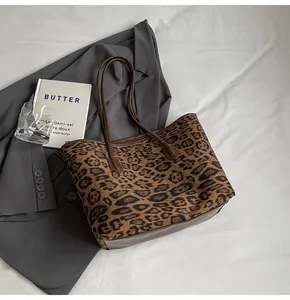 Flat lay of a leopard print tote bag with brown straps on a white fabric background