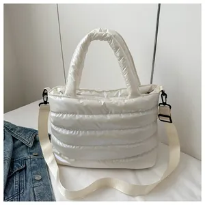 Detail of white quilted puffer bag with detachable strap and glossy finish shown with denim