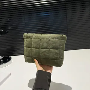 Vista detallada de neceser de terciopelo acolchado verde oscuro sostenido en la mano