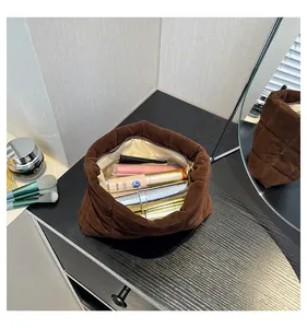 Detalle de la bolsa de cosméticos de terciopelo acolchado marrón con maquillaje en mesa