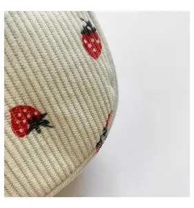 Detailed close-up of cream corduroy fabric with high-quality red strawberry embroidery