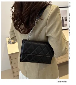 Detail of black quilted leather shoulder bag with silver chain strap worn by a model