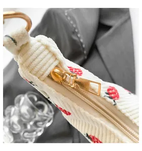 Detail of off-white corduroy crescent bag featuring red cherry prints and gold zipper hardware